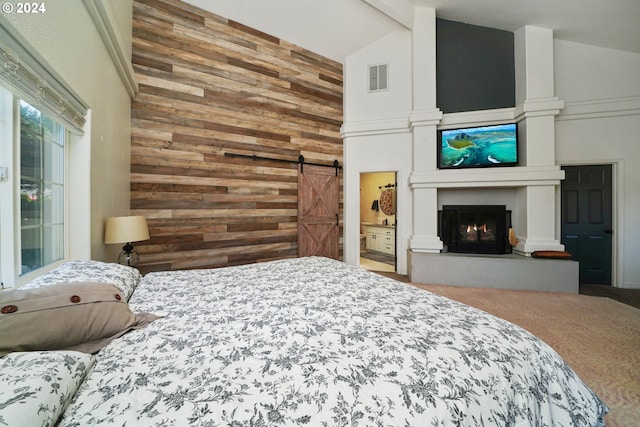 bedroom with carpet, ensuite bath, a barn door, high vaulted ceiling, and wood walls