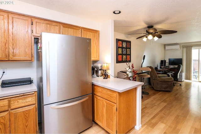 kitchen featuring light wood-type flooring, kitchen peninsula, a wall mounted air conditioner, ceiling fan, and stainless steel fridge