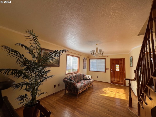 living room featuring light hardwood / wood-style floors, a chandelier, a textured ceiling, and ornamental molding