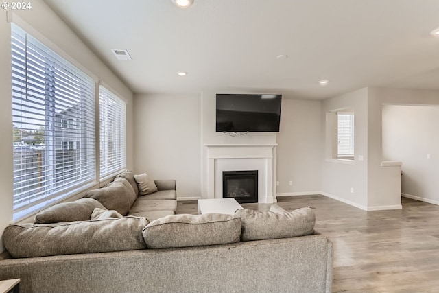 living area with a wealth of natural light, a glass covered fireplace, wood finished floors, and recessed lighting