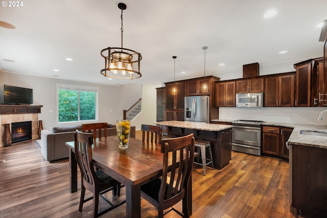 dining room with ornamental molding, sink, a notable chandelier, dark hardwood / wood-style floors, and a tiled fireplace