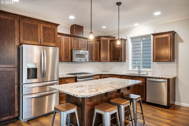 kitchen with appliances with stainless steel finishes, sink, dark hardwood / wood-style floors, a kitchen island, and hanging light fixtures