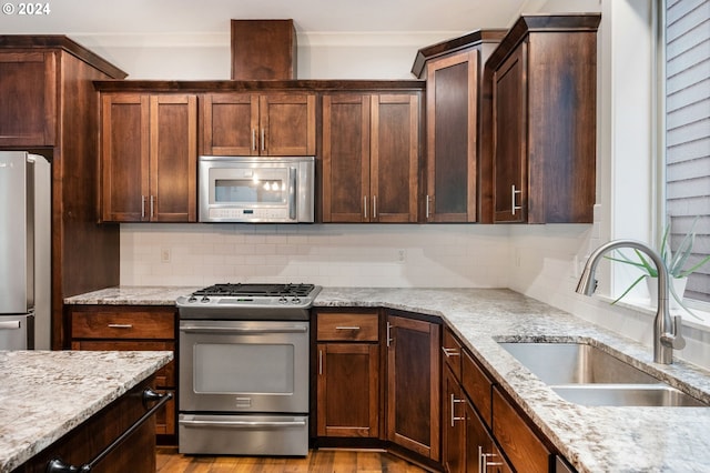 kitchen with light stone countertops, stainless steel appliances, light hardwood / wood-style floors, and sink