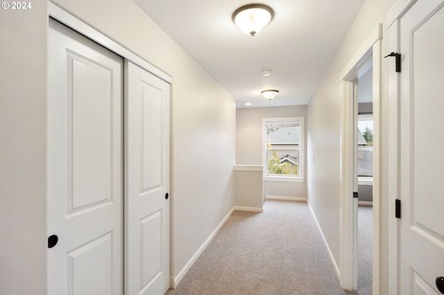 hallway with a textured ceiling and light colored carpet