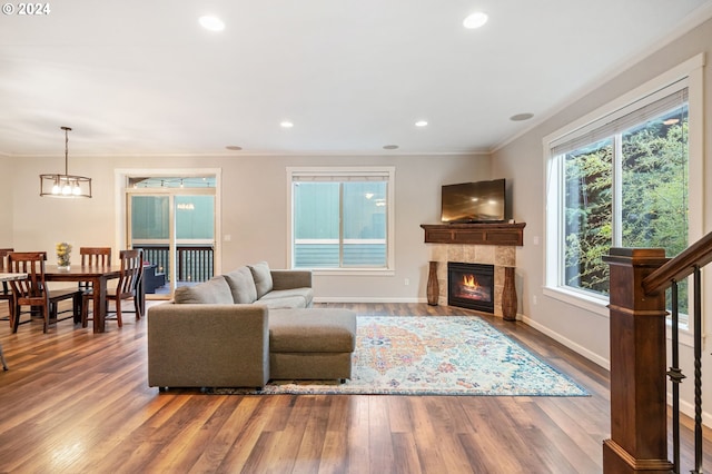 living room with wood-type flooring, an inviting chandelier, crown molding, and a tiled fireplace