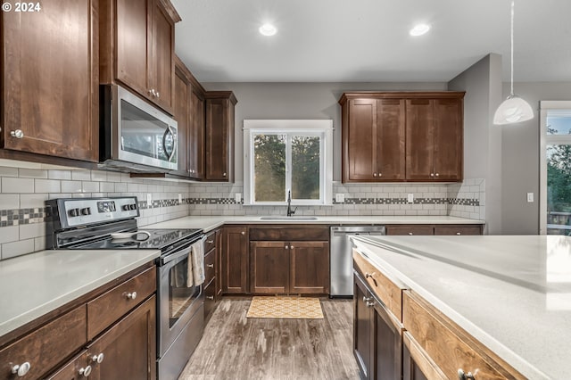 kitchen with appliances with stainless steel finishes, hanging light fixtures, dark wood-type flooring, tasteful backsplash, and sink