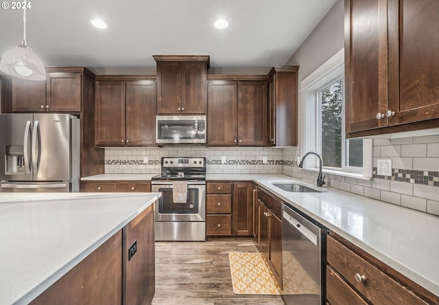 kitchen with light hardwood / wood-style floors, tasteful backsplash, sink, stainless steel appliances, and decorative light fixtures