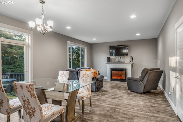 dining area featuring a tile fireplace, wood-type flooring, and an inviting chandelier