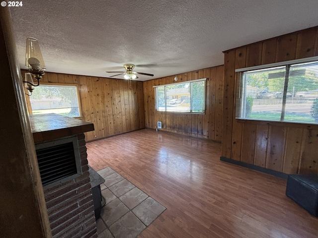 unfurnished living room with wood walls, a textured ceiling, hardwood / wood-style flooring, and ceiling fan