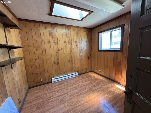 spare room featuring a textured ceiling, wooden walls, light hardwood / wood-style floors, and baseboard heating