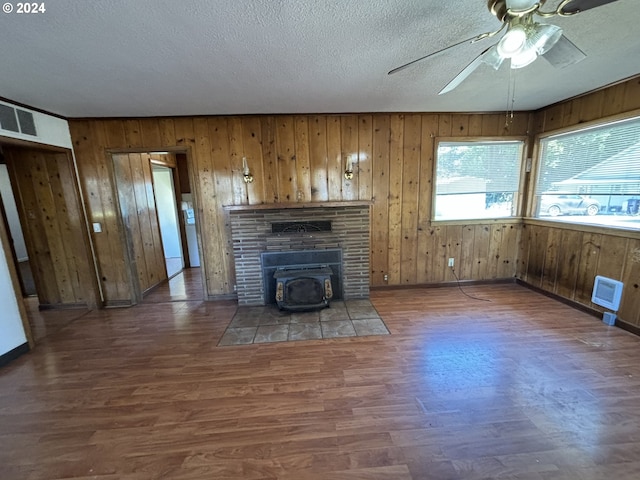 unfurnished living room featuring wooden walls, a textured ceiling, dark wood-type flooring, ceiling fan, and a fireplace