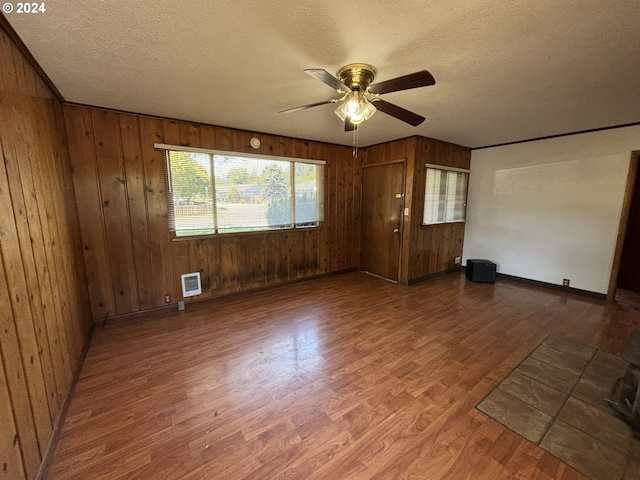 unfurnished bedroom featuring ceiling fan, wood walls, hardwood / wood-style floors, and a textured ceiling