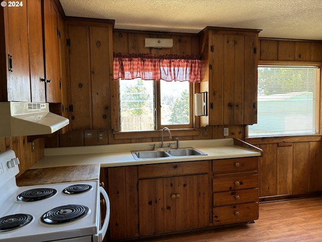 kitchen with stove, light hardwood / wood-style flooring, sink, a textured ceiling, and wood walls