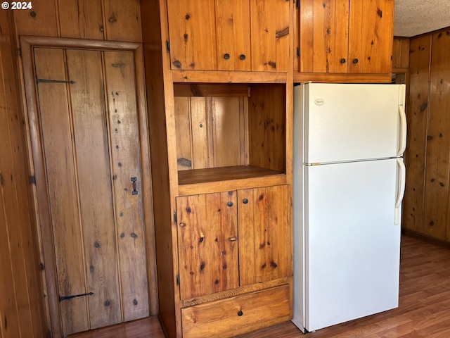 kitchen featuring wood walls, a textured ceiling, hardwood / wood-style flooring, and white refrigerator