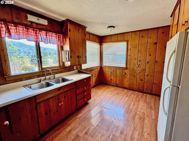 kitchen featuring sink, white refrigerator, wooden walls, and light wood-type flooring