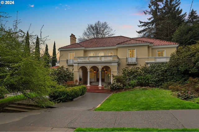 mediterranean / spanish home featuring a tiled roof, a balcony, a chimney, and stucco siding