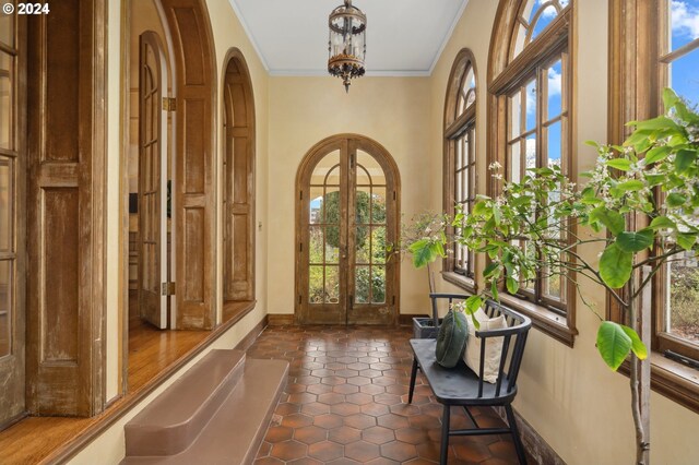 foyer entrance with crown molding, french doors, plenty of natural light, and an inviting chandelier