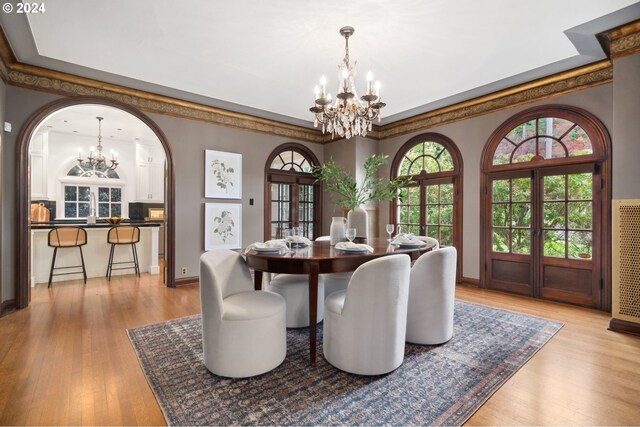 dining room featuring light wood-type flooring, a chandelier, crown molding, and french doors