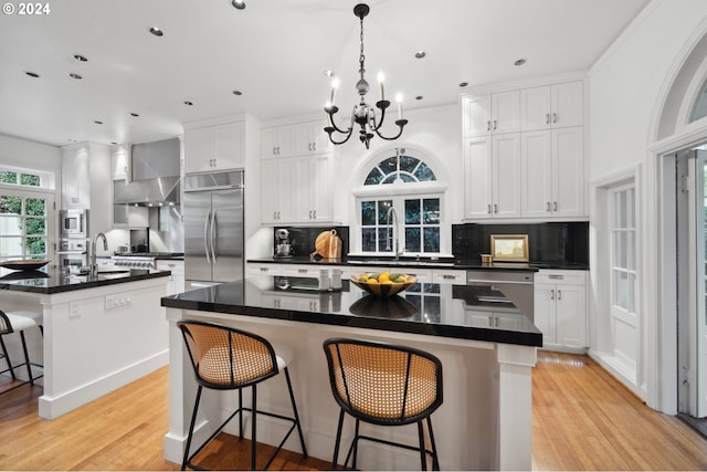 kitchen featuring a center island with sink, built in appliances, a kitchen bar, and white cabinets