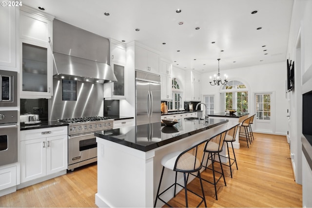 kitchen with built in appliances, light wood-type flooring, white cabinetry, and a kitchen island with sink