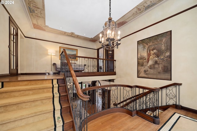 staircase featuring crown molding, wood-type flooring, and a chandelier