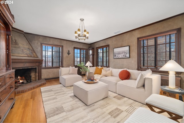 living room with light wood-type flooring, a fireplace, a notable chandelier, and ornamental molding