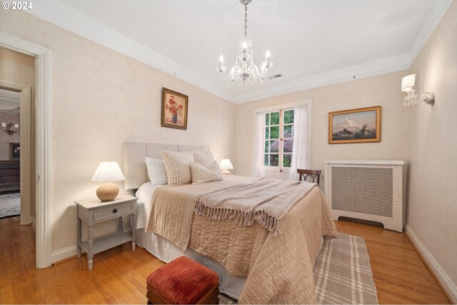 bedroom featuring light hardwood / wood-style flooring, ornamental molding, radiator heating unit, and a notable chandelier