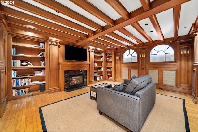 living room with built in shelves, wooden walls, a premium fireplace, beam ceiling, and light hardwood / wood-style floors