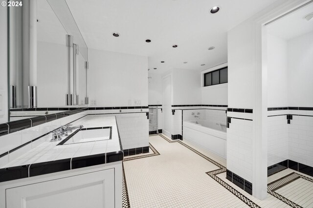 kitchen with tile countertops, light tile patterned floors, sink, tile walls, and white cabinets