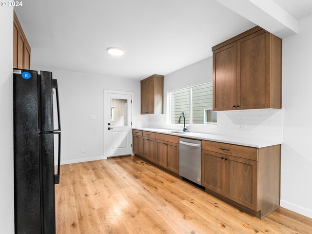 kitchen with black fridge, backsplash, sink, stainless steel dishwasher, and light hardwood / wood-style flooring