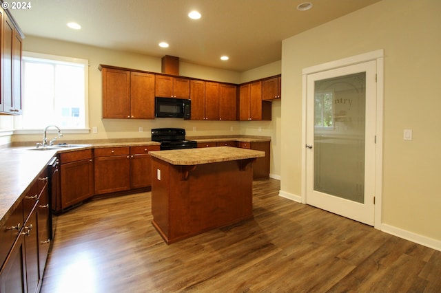 kitchen with dark wood-type flooring, a breakfast bar area, sink, a kitchen island, and black appliances