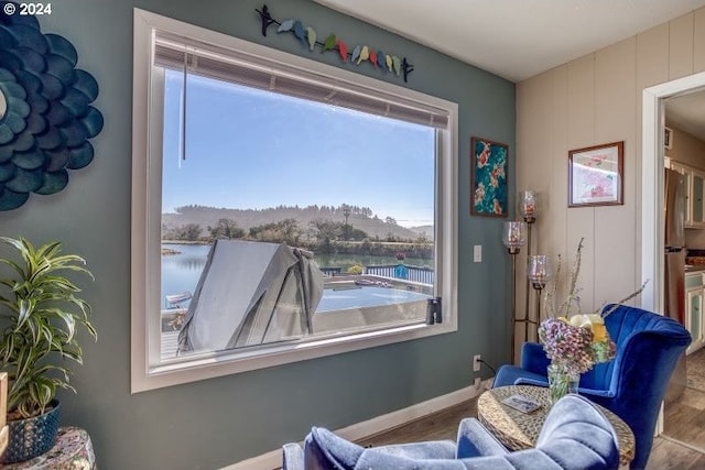 sitting room with a water view, baseboards, and wood finished floors