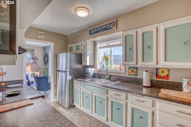 kitchen with a sink, white cabinets, freestanding refrigerator, dark countertops, and glass insert cabinets