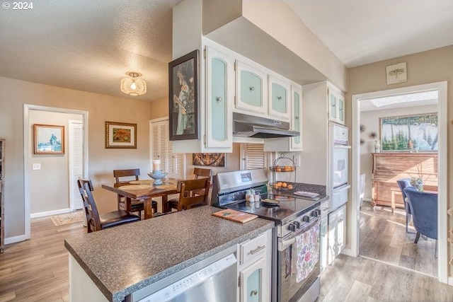 kitchen featuring dark countertops, under cabinet range hood, white cabinetry, and stainless steel appliances