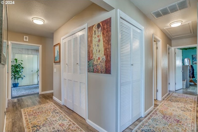 hall featuring a textured ceiling, wood finished floors, visible vents, and baseboards