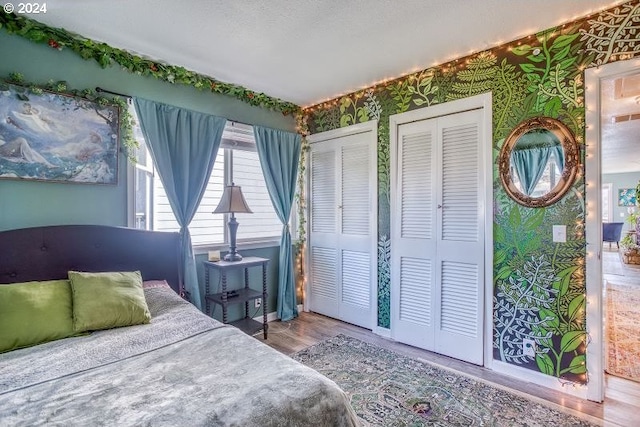 bedroom with wallpapered walls, a textured ceiling, two closets, and wood finished floors