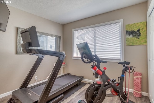 workout area with light wood-style floors, baseboards, and a textured ceiling