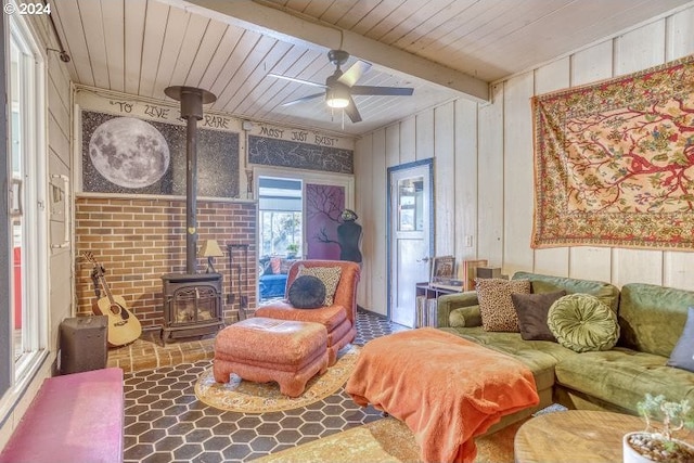 living area with a ceiling fan, wood ceiling, a wood stove, and beamed ceiling