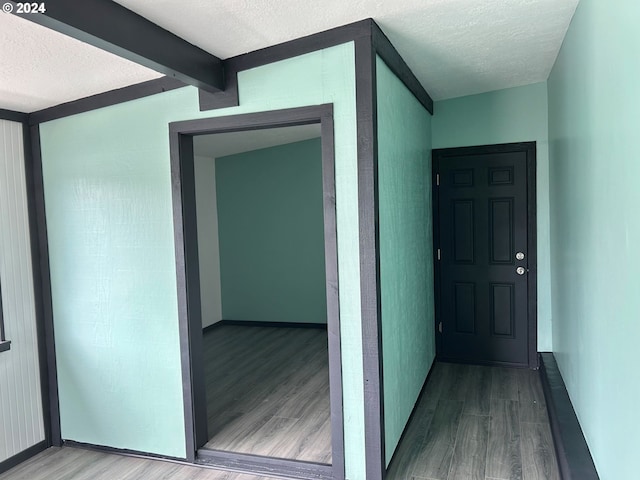 hall featuring a textured ceiling, wood finished floors, and beam ceiling