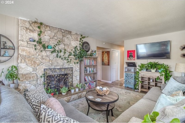 living room with light wood-style flooring, a stone fireplace, and a textured ceiling