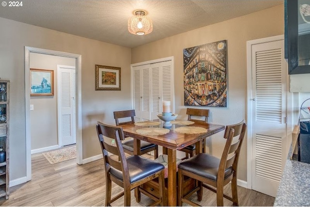 dining room with a textured ceiling, light wood-type flooring, and baseboards