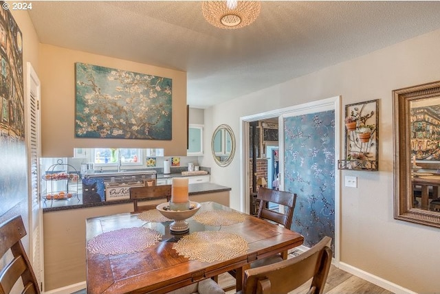 dining space with a textured ceiling, light wood-type flooring, and baseboards