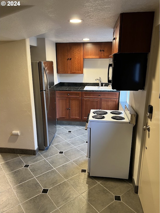 kitchen featuring stainless steel refrigerator, sink, white electric range oven, dark tile patterned floors, and a textured ceiling