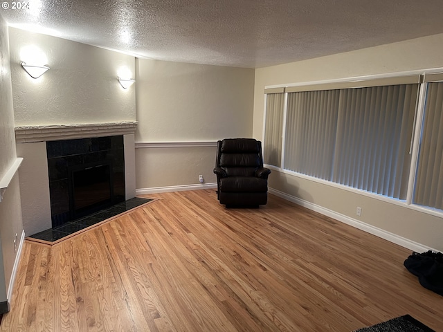 unfurnished room featuring a tiled fireplace, wood-type flooring, and a textured ceiling