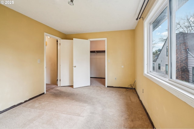 unfurnished bedroom with a walk in closet, light colored carpet, a closet, and multiple windows