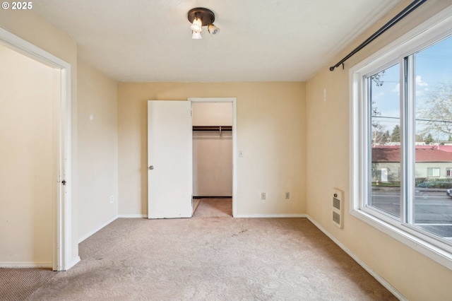 unfurnished bedroom featuring light colored carpet, a closet, heating unit, and a walk in closet