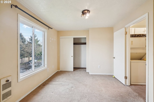 unfurnished bedroom with stacked washer / dryer, heating unit, and light carpet