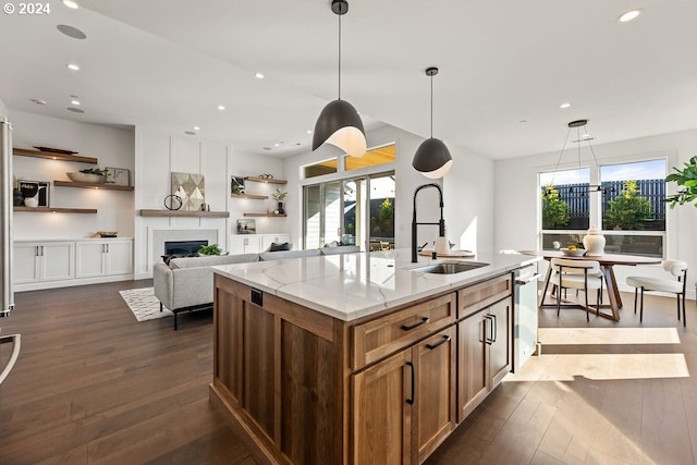 kitchen with sink, light stone countertops, hanging light fixtures, and a center island with sink