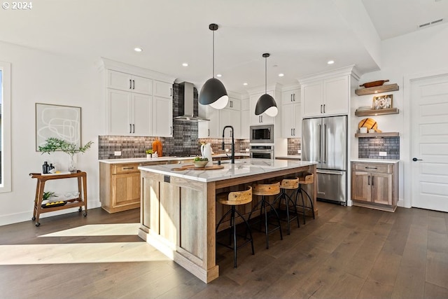 kitchen featuring stainless steel appliances, white cabinetry, a center island with sink, and wall chimney range hood