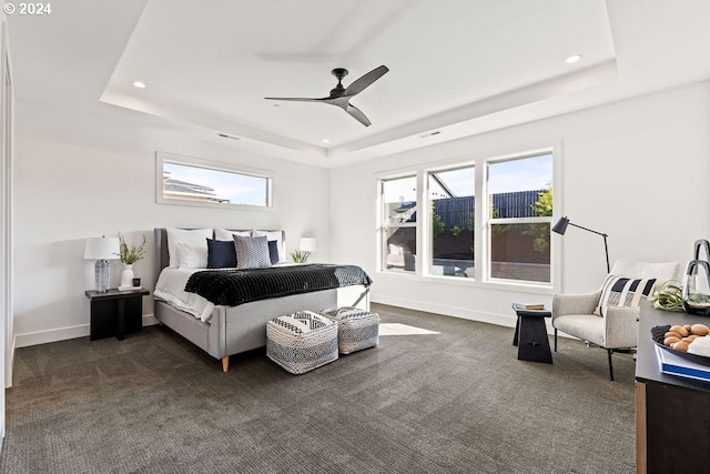 bedroom with a raised ceiling, ceiling fan, and dark colored carpet